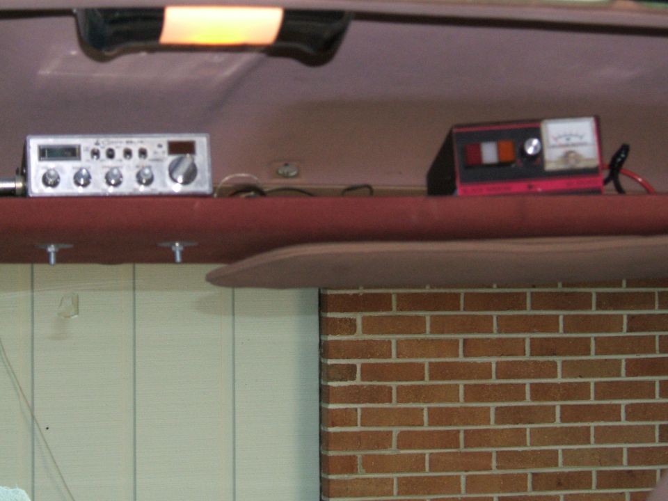 CB radio and battery charger mounted on a red shelf inside a vehicle