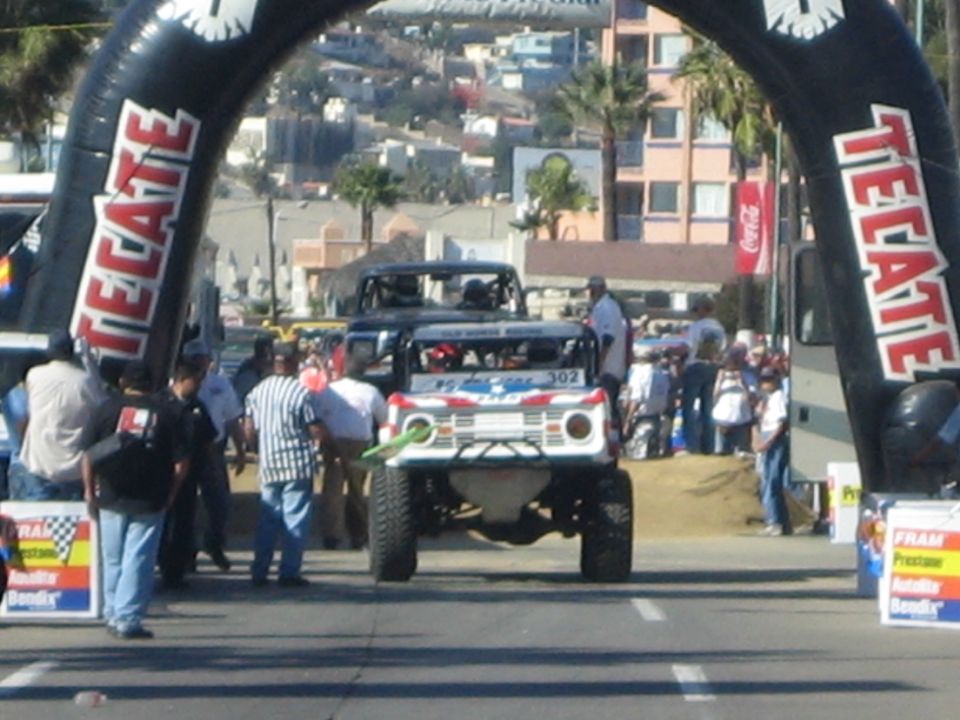 Race truck passing under a Tecate inflatable arch with crowd watching