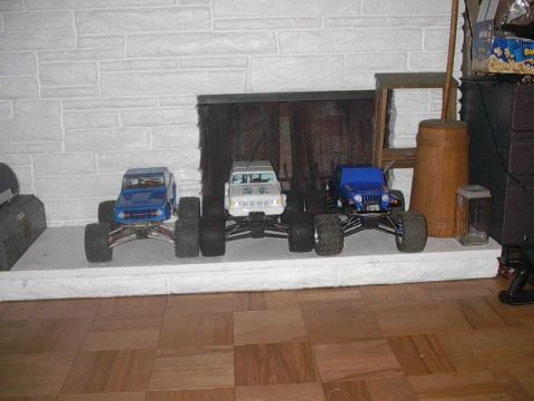 1993 Ford Bronco - Three remote-controlled monster trucks are displayed on a white hearth in front of a brick fireplace.
