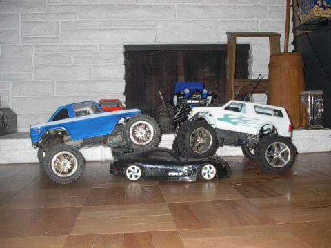 1993 Ford Bronco - Several remote-controlled vehicles are arranged on a wooden floor in front of a fireplace.