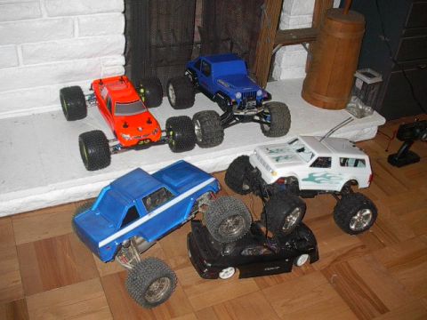 1993 Ford Bronco - A collection of RC monster trucks, including a blue pickup and a white SUV, are displayed indoors.