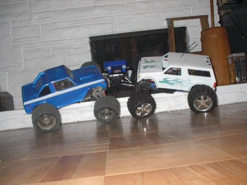 1993 Ford Bronco - A collection of RC monster trucks, including a blue Bronco-style truck and a white SUV, are displayed indoors.