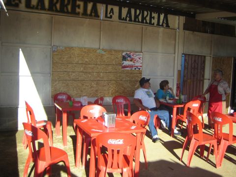 1990 Ford Bronco - open-air eatery signed La Carreta with red Coca-Cola plastic tables and chairs, a couple seated and an apron-clad worker standing.