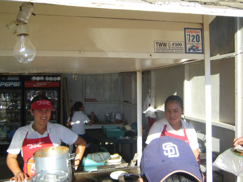 Two women in red aprons at a roadside food stand under a TWW #300 decal