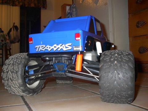 1993 Ford Bronco - Rear view of a blue Traxxas RC monster truck with oversized tires and orange shock absorbers.