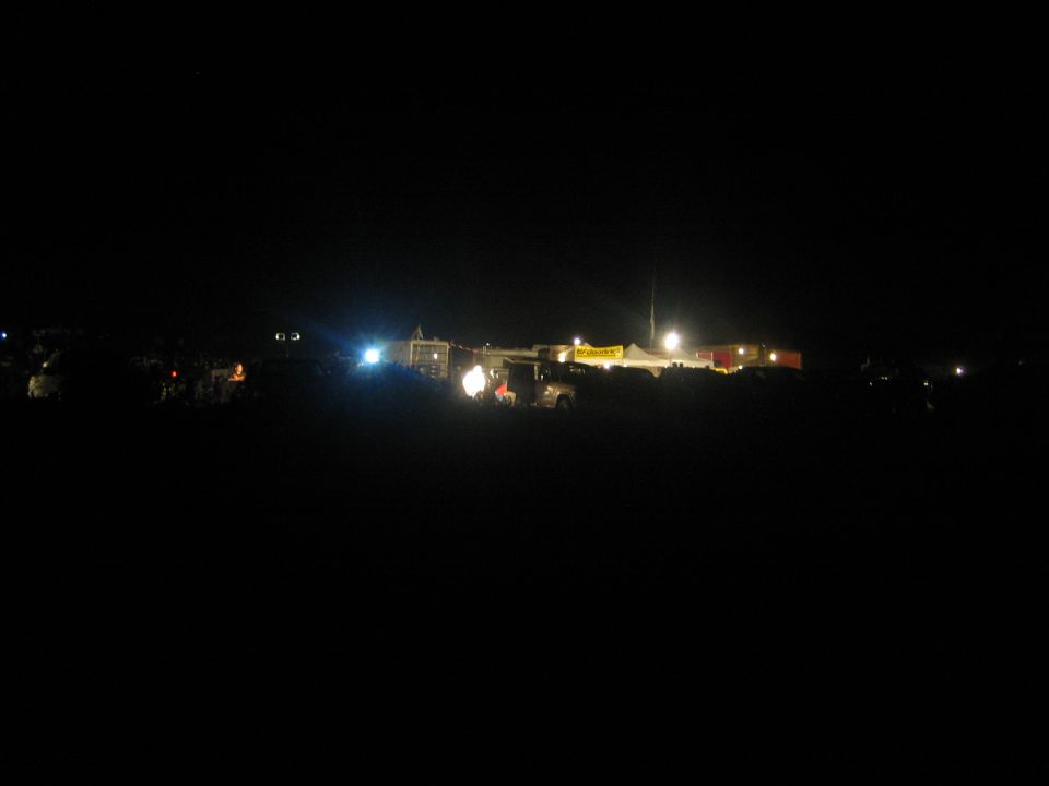 Distant nighttime race pits with floodlights and tents in the dark