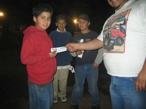 1990 Ford Bronco - man in a monster-truck t-shirt hands a TWW #300 card to three boys gathered outdoors at night.