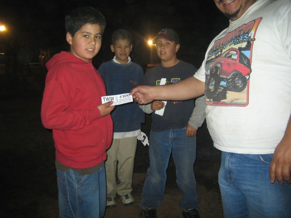 Three boys and a man holding TWW #300 cards outdoors at night