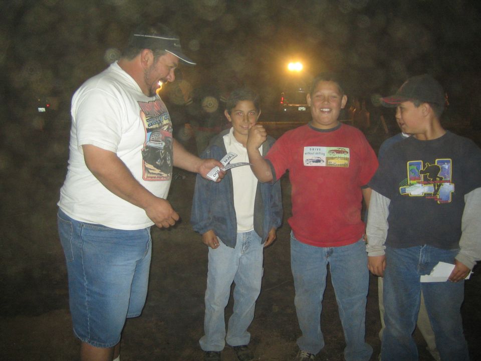 Man in white tee with three boys outdoors at night under a light