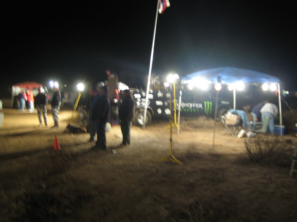 Crowd at a floodlit desert race pit with Monster Energy canopy at night