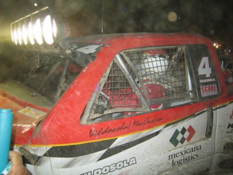 1990 Ford Bronco - Close view of the red number 4 Vildosola/MacCachren trophy truck cab with caged window and roof light bar at night.