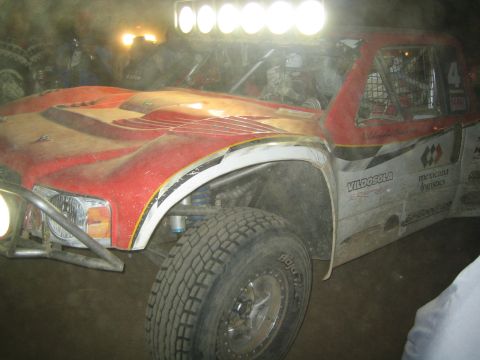 1990 Ford Bronco - dirt-caked front end of the red and white number 4 Vildosola trophy truck with light bar glowing at night.