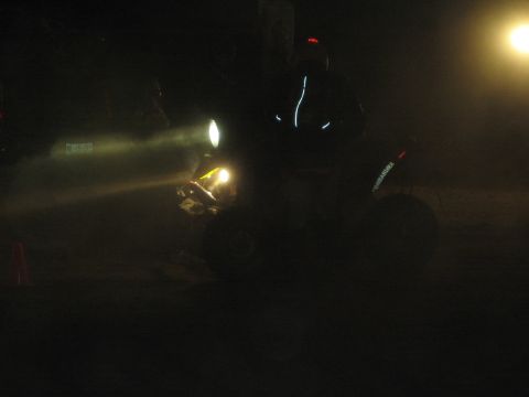 1990 Ford Bronco - quad ATV with its headlight glowing and a reflective-jacketed rider sits in near-darkness at night.