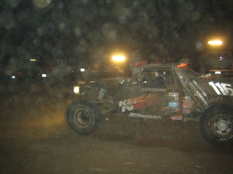 1990 Ford Bronco - off-road race truck with orange flame graphics, K&N and BFGoodrich decals and number 116 kicks up dust racing at night.