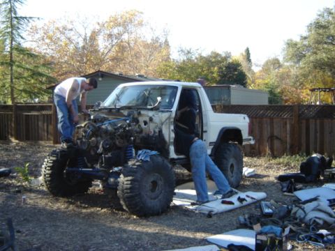 1991 Ford Bronco - Two individuals are working on a white 1991 Ford Bronco that has had its engine removed.