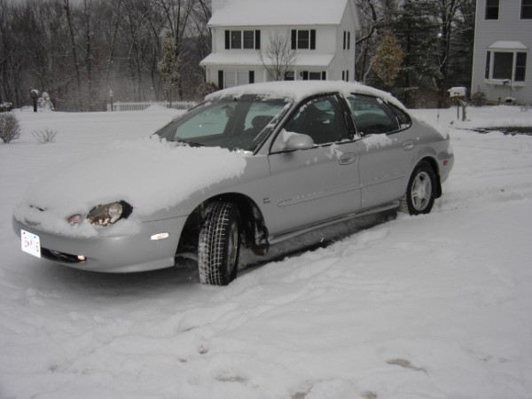 Silver 1999 Ford Taurus covered in snow, parked in a driveway