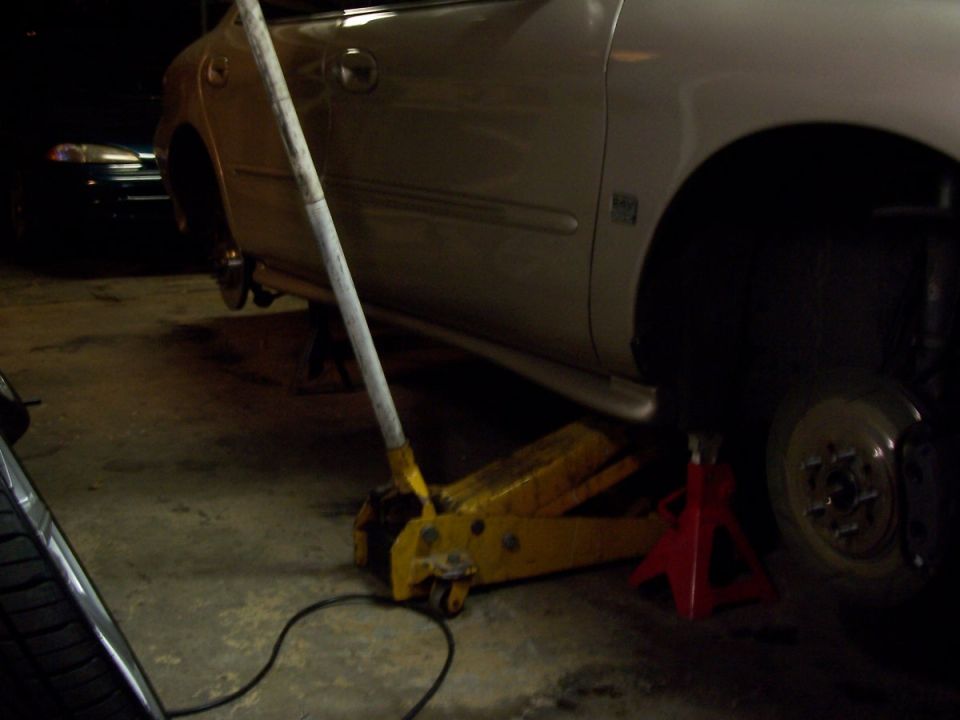Silver sedan on jack stands with a yellow floor jack, rear wheel removed
