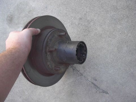 1993 Ford Bronco - Brake rotor and hub assembly held by a hand against a concrete surface.