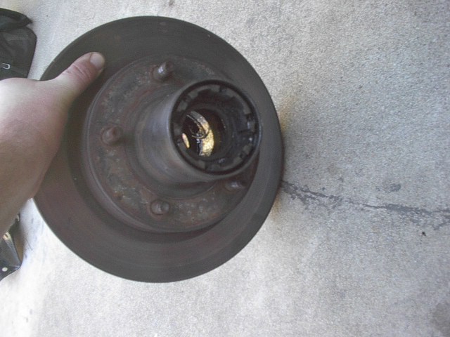 Hand holding a vehicle's brake rotor and hub assembly. The hub has a locking mechanism visible inside