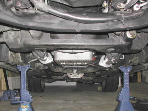 1993 Ford Thunderbird - The underside of a vehicle is shown, supported by jack stands, revealing the exhaust system and transmission components.