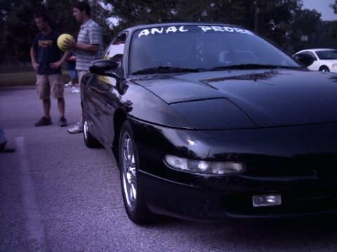 1995 Ford Probe - A black car with custom text on its windshield is parked outdoors, with people standing nearby.