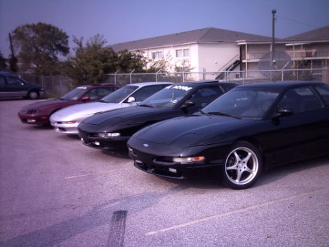 1995 Ford Probe - Several Ford Probe models are lined up in a parking lot, with buildings in the background.