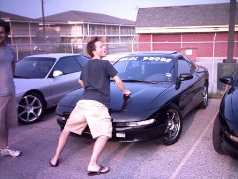1995 Ford Probe - A black coupe with a banner reading "PROBE" is parked in a lot next to a silver car, with two men nearby.