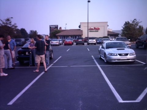 1995 Ford Probe - A silver coupe with a prominent hood scoop is parked in a lot with other vehicles and people.