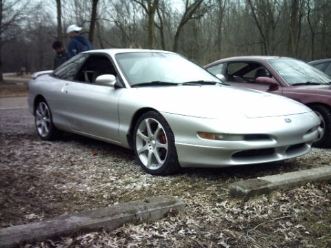 1995 Ford Probe - A silver 1995 Ford Probe is parked next to another vehicle in a wooded area.