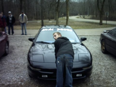 1995 Ford Probe - A person interacts with a black sports car parked outdoors with other vehicles and people nearby.