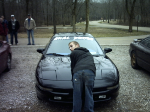 Black Ford Probe front view with ANAL PROBE windshield banner, person leaning on hood
