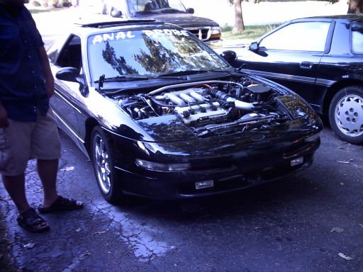 Black coupe with hood up showing V6 engine and ANAL PROBE windshield banner in a driveway