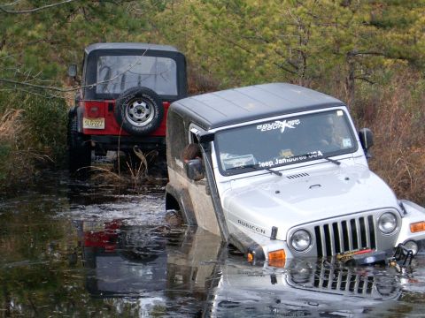 1986 Ford F-250 - Two Jeeps navigate through a watery off-road course, with one vehicle significantly submerged.
