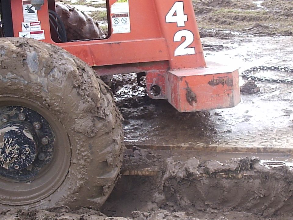 Orange telehandler forklift wheel and counterweight stuck in deep mud, number 42 on boom