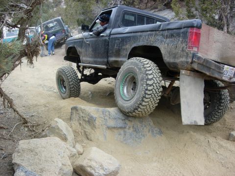 1987 Ford Bronco - A black pickup truck navigates a challenging rocky terrain with other vehicles in the background.