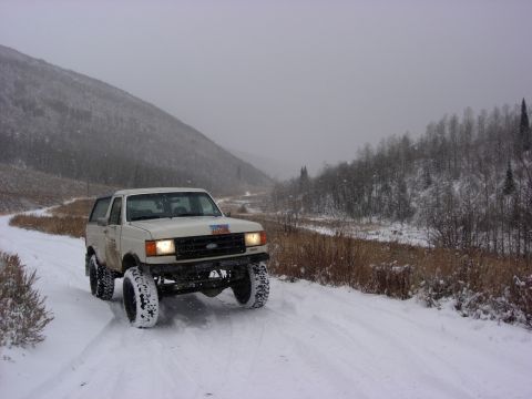 1987 Ford Bronco - White 1987 Ford Bronco navigates a snowy mountain road during a snowfall.