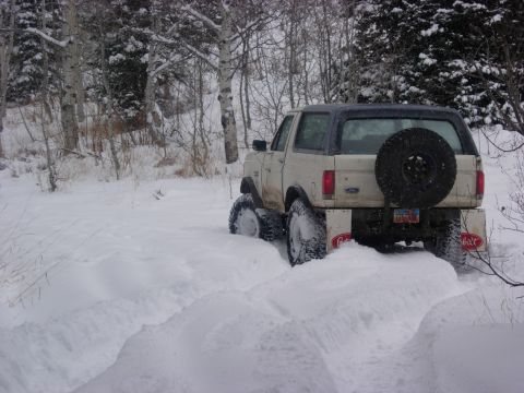 1987 Ford Bronco - Ford Bronco navigates a snowy trail, showing its rear profile and spare tire mounted externally.