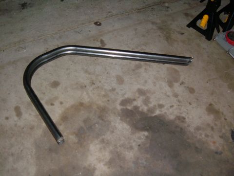 1985 Ford Ranger - A bent metal tube, possibly a section of a roll bar, lies on a concrete floor with some oil stains.