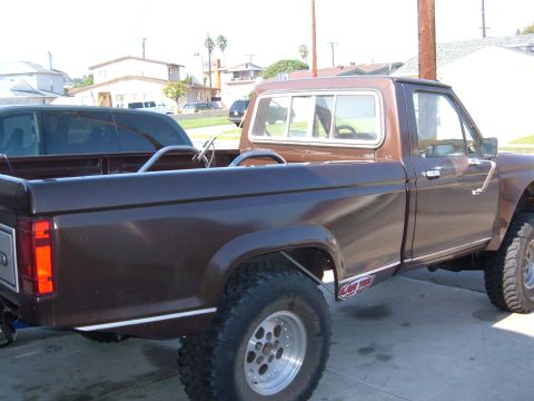 1985 Ford Ranger - A lifted brown pickup truck with racing wheels and chrome trim is parked on a paved surface.