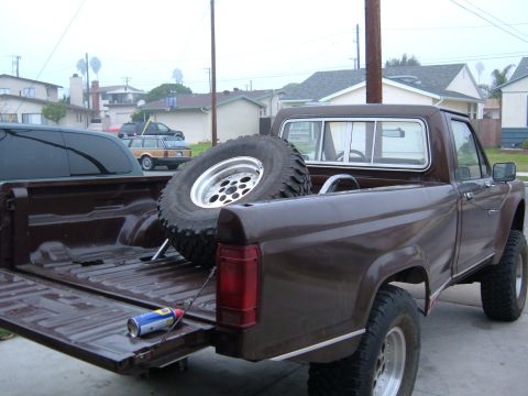 1985 Ford Ranger - A brown pickup truck is parked in a residential area, showing its bed with a spare tire and a can of spray paint.
