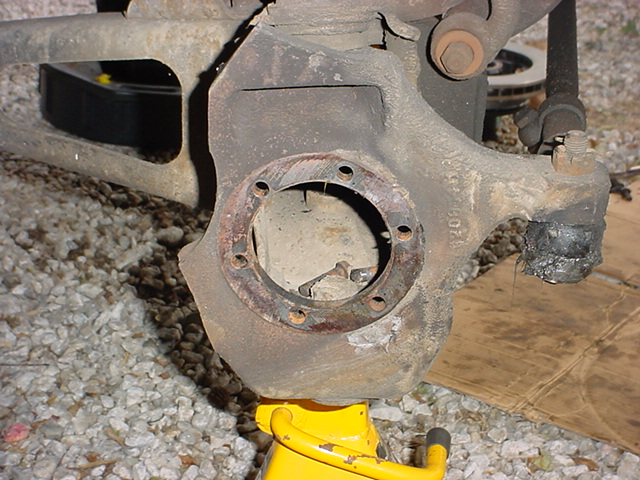 Front axle knuckle with spindle removed exposing the bore, supported on a yellow jack stand