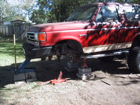 1990 Ford Bronco - A red 1990 Ford Bronco with a tan stripe is raised on jack stands for maintenance.