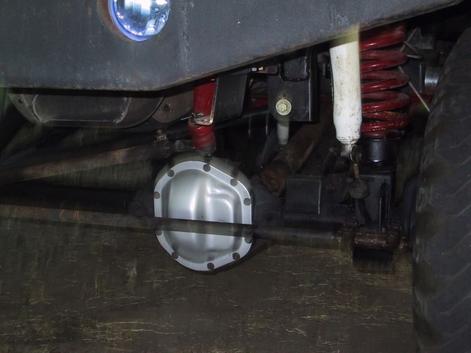 Underneath view of a vehicle's rear axle, differential cover, red coil springs, and shocks
