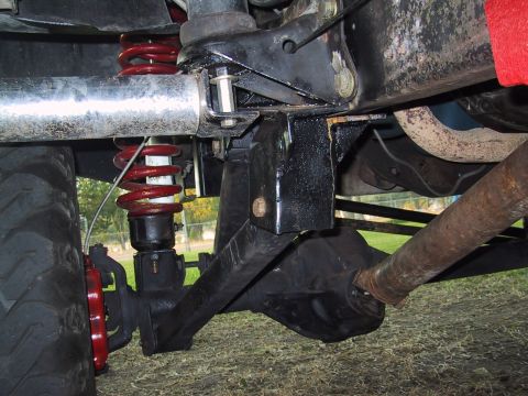 1990 Ford Bronco - Close-up view of the suspension system and undercarriage of a vehicle, showing red coil springs and a large tire.