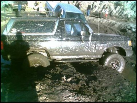 1988 Ford Bronco - A muddy 1988 Ford Bronco navigates a difficult off-road terrain.