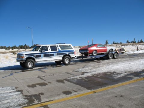 1994 Ford C-350 (Centurion Conversions) - A white and blue 1994 Ford C-350 Centurion conversion SUV is seen towing a red car on a trailer during a trip.