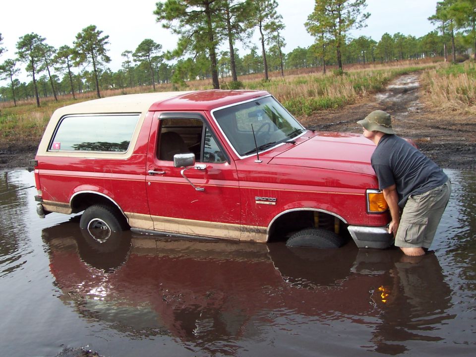 Red SUV stuck in mud, person pushing