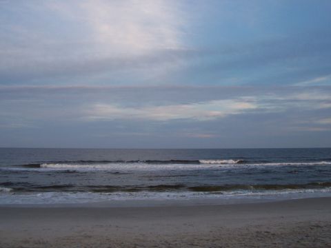 1989 Ford Bronco - A tranquil beach scene unfolds under a sky filled with soft clouds, with gentle waves lapping the shore.