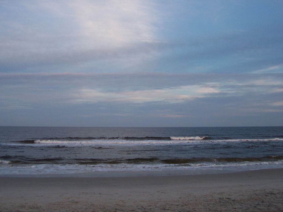 Beach with ocean waves under a cloudy sky, and a Supermotors.net watermark