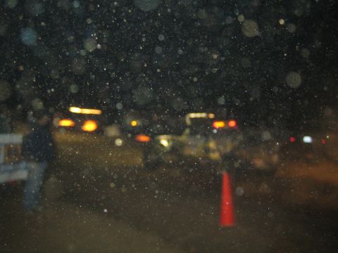 1990 Ford Bronco - very dark night scene shows blurred amber and red vehicle lights and an orange traffic cone amid floating dust specks.